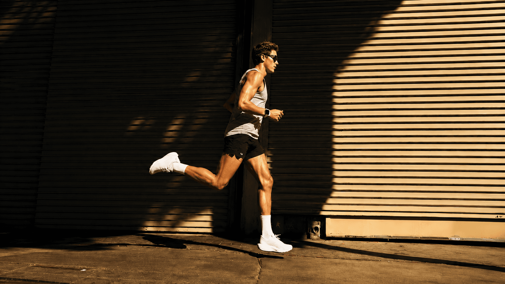 An athlete running past a sunlit corrugated wall at golden hour