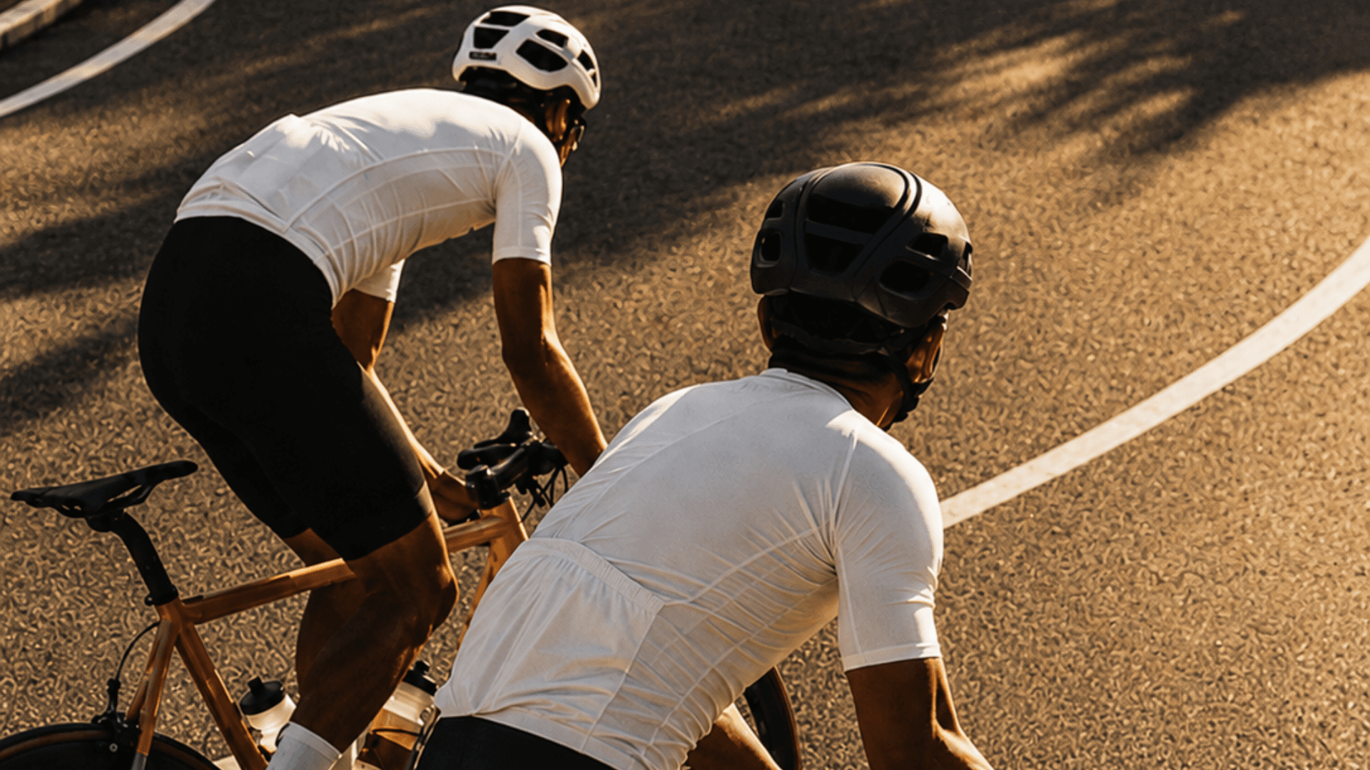 Two road cyclists riding a curving road at golden hour.